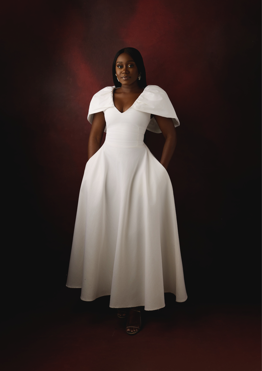 Woman wearing a white dress with a cape-like top against a dark background